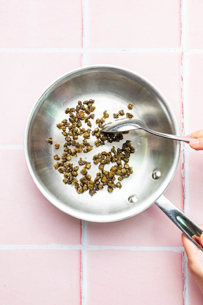 hand stirring fried capers in pan