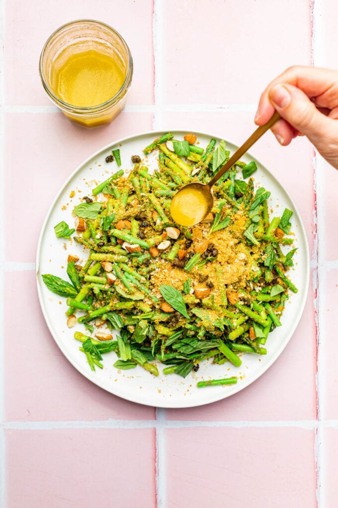hand drizzling dressing on cold asparagus salad